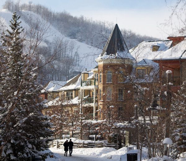 2 people walking down a village streetscape in the winter with ski hills in background